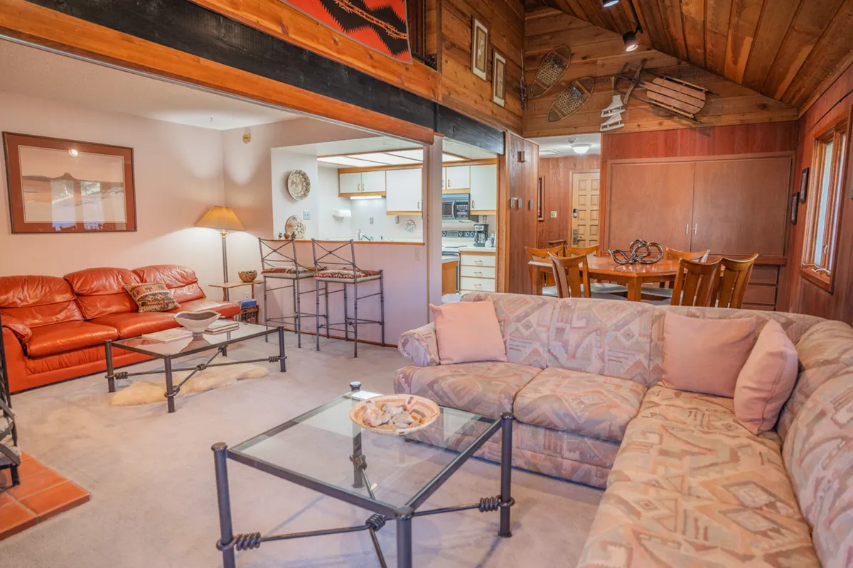 A welcoming interior living area with red leather sofas around a glass coffee table, a wooden dining table set for meals, and decorative wall art creating a comfortable, homey atmosphere ideal for families and groups.