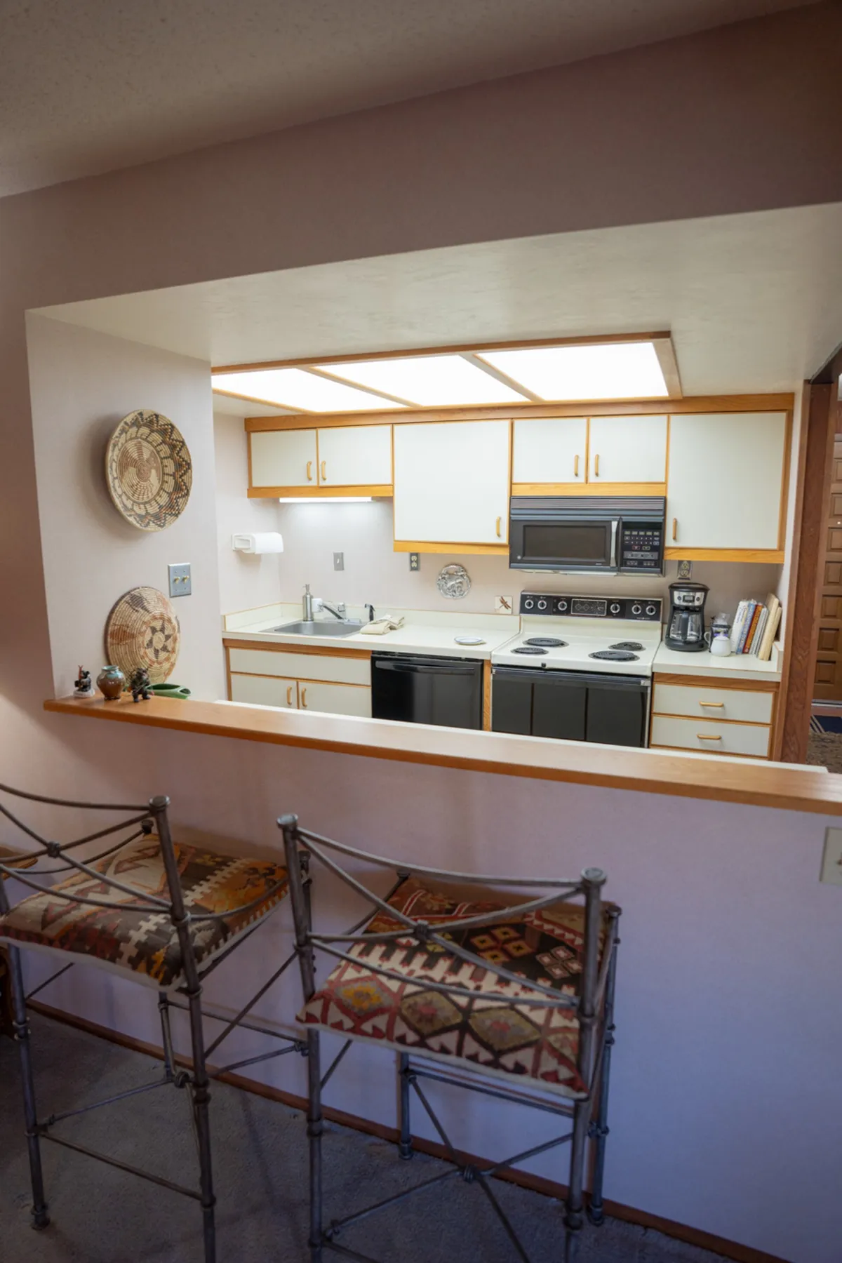 A view of the kitchen area with a kitchen island, bar stools, modern appliances, and decorative plates on the wall. The setup invites guests to cook, gather, and socialize, highlighting the kitchen’s role as a hub for family meals and gatherings.