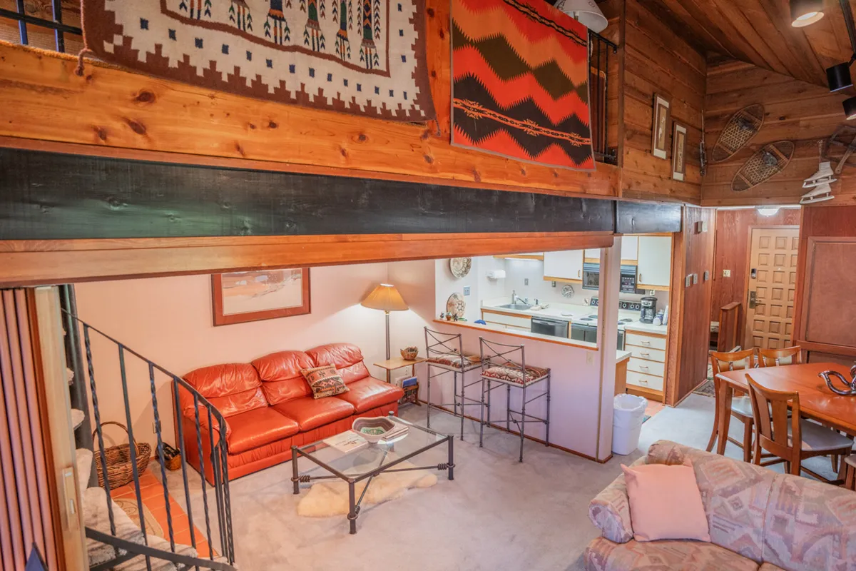 This scene showcases a comfortable living area with a red leather sofa, glass coffee table, textile wall hangings, and a wooden dining table beyond. The room exudes warmth and encourages relaxation, conversation, and shared activities.