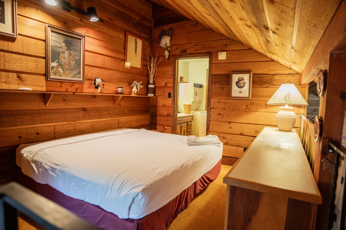 Here, a cozy bed is set against warm wood paneling, accompanied by a soft lamp and tasteful wall art. The room feels inviting and intimate, emphasizing relaxation and a peaceful night's sleep.