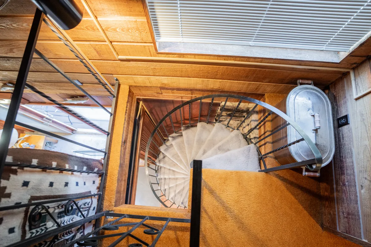 This image features a spiral staircase leading up toward a wooden ceiling with a prominent skylight above, filling the space with natural light. The staircase and the presence of the skylight evoke a sense of verticality and openness, suggesting an upper-level loft area connected to the main living space below.