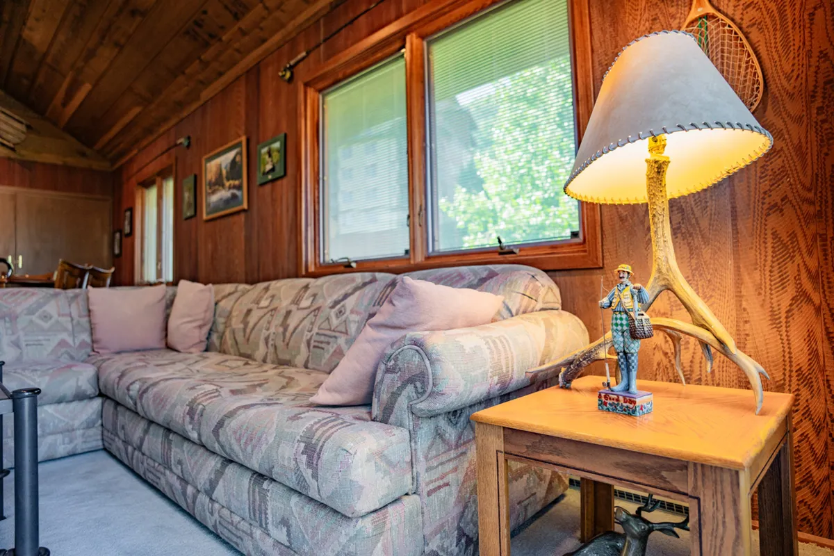 A cozy seating area with a sofa, lamp, and decorative figurine is positioned in front of large windows. Sunlight floods the loft-like area, and the arrangement hints at a quiet, inviting space perfect for relaxing, reading, or enjoying the view below.