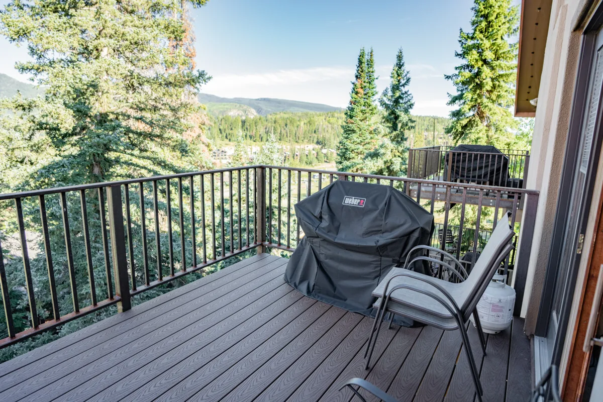 The exterior hero image showcases a private deck framed by a sturdy railing, complete with a grill cover and cozy seating area, all nestled among tall pine trees. The scene evokes a sense of relaxing outdoors, perfect for enjoying the fresh Colorado mountain air, with opportunities for barbecuing, stargazing, and socializing with family and friends amid serene natural surroundings.